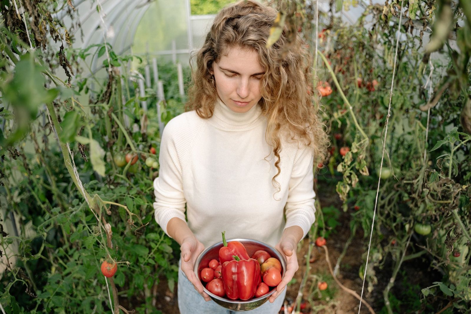 Caucasian woman holding freshly harvested vegetables in a greenhouse, showcasing organic farming.