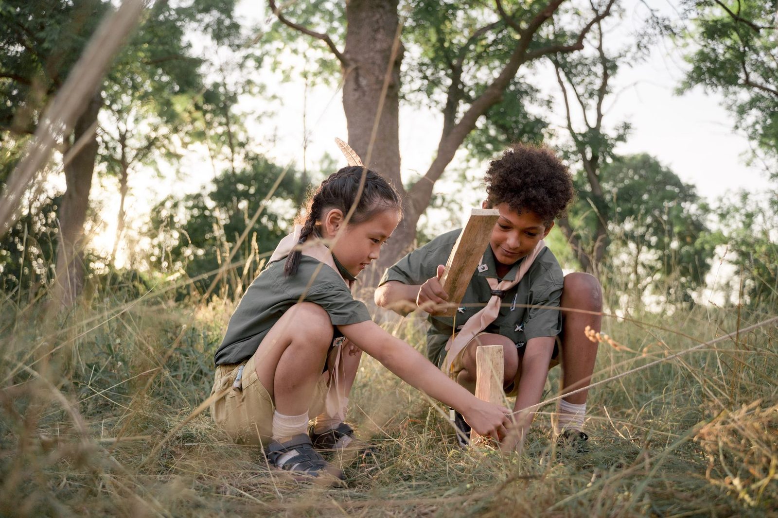Two kids at a scouting camp, learning teamwork with woodcraft outdoors.