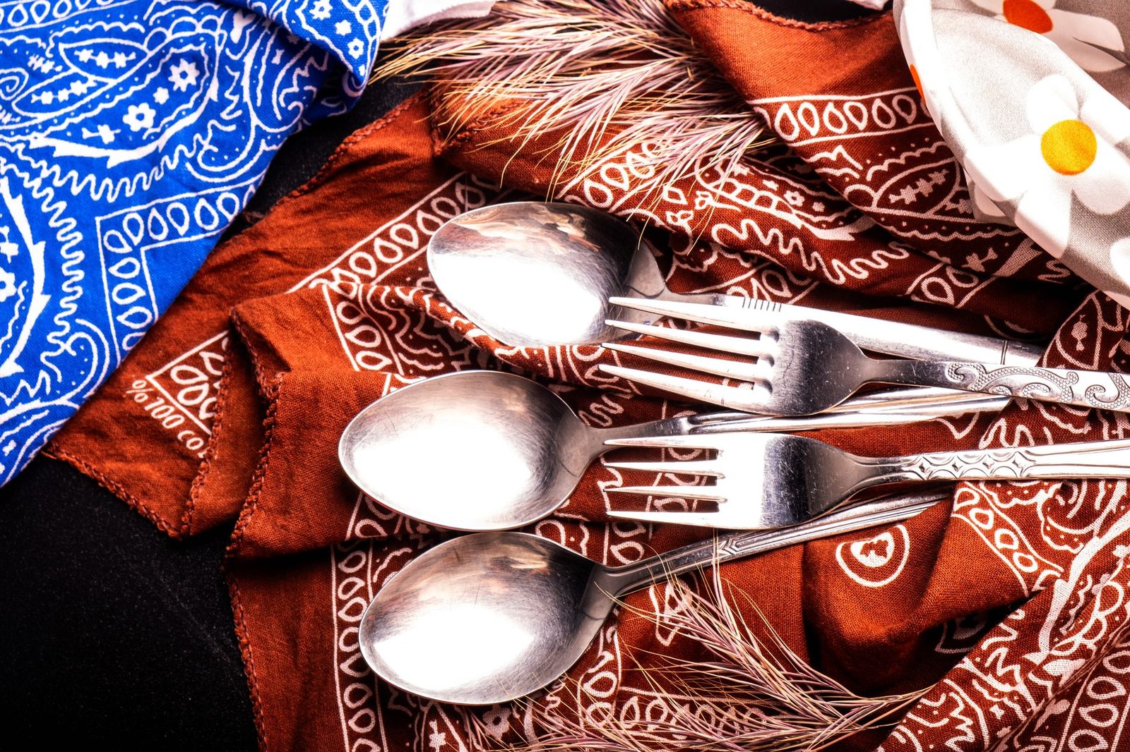 An artistic close-up of silver cutlery and vibrant bandanas in a flat lay.