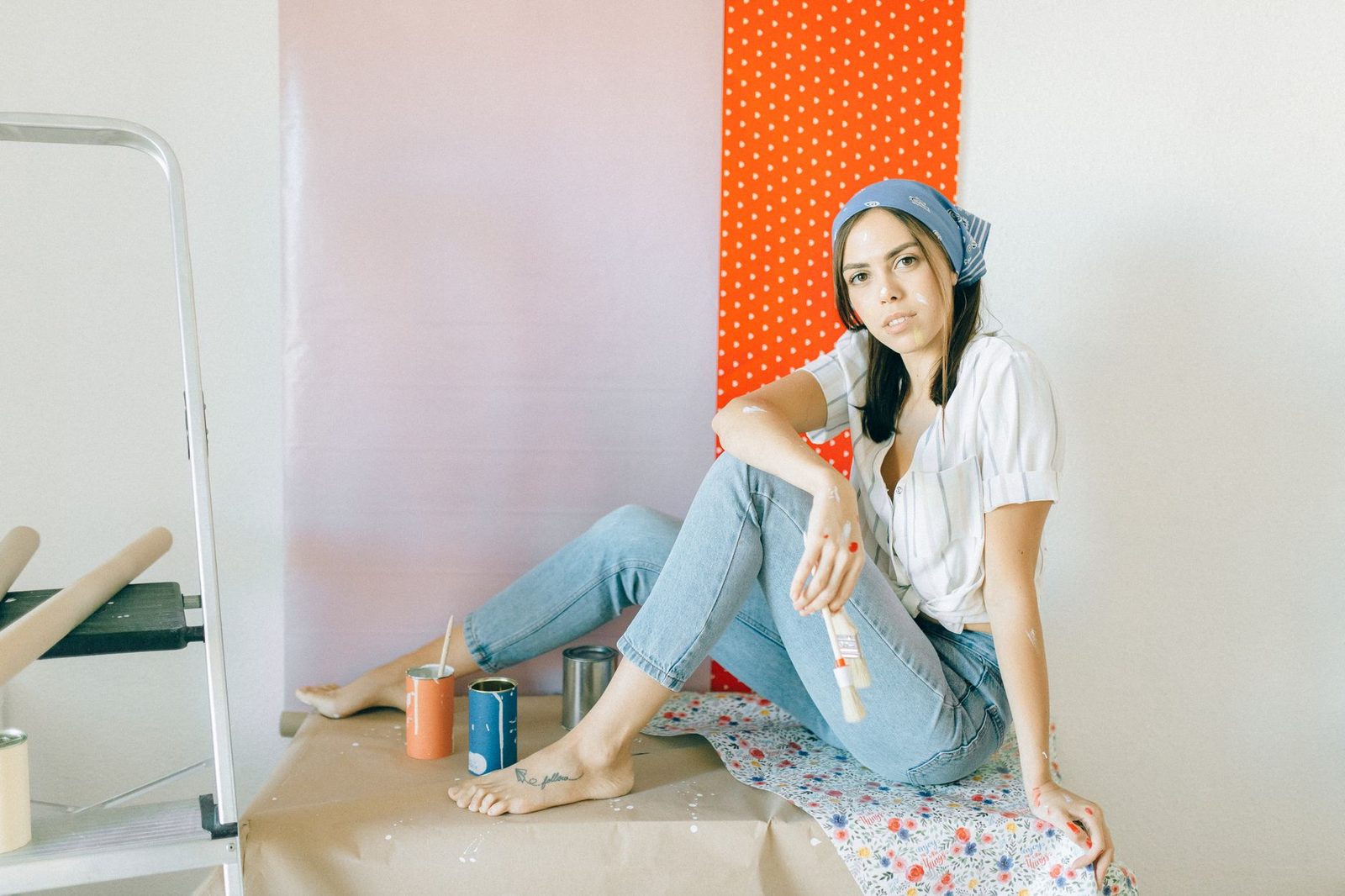 Young woman sitting casually with paintbrush amid DIY home project setting.