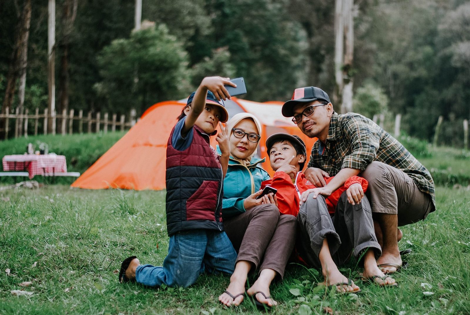 Family enjoying a camping trip, taking a selfie in front of their tent during the day.