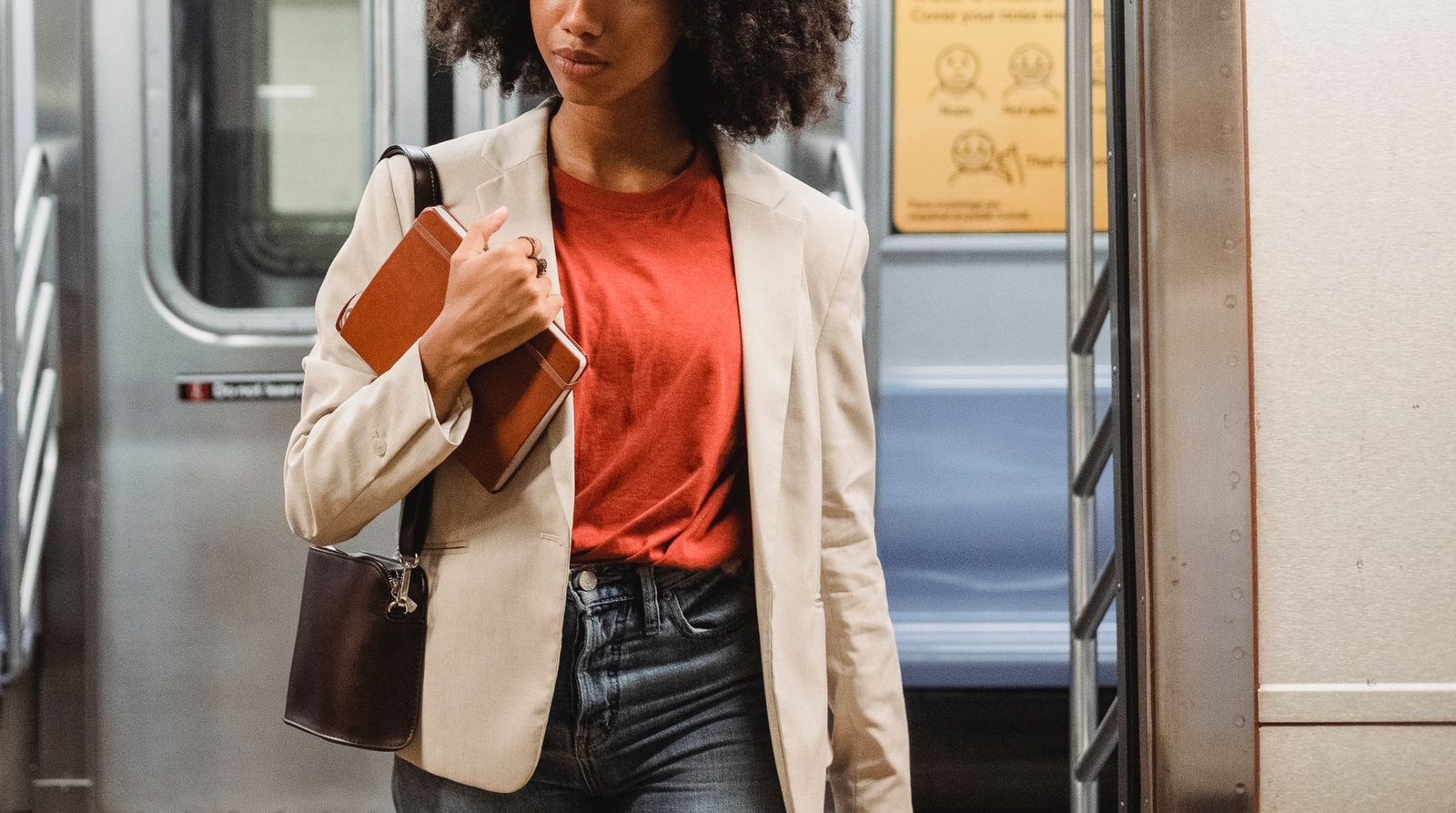 Confident woman in a blazer with notebook and purse walking in a subway train.