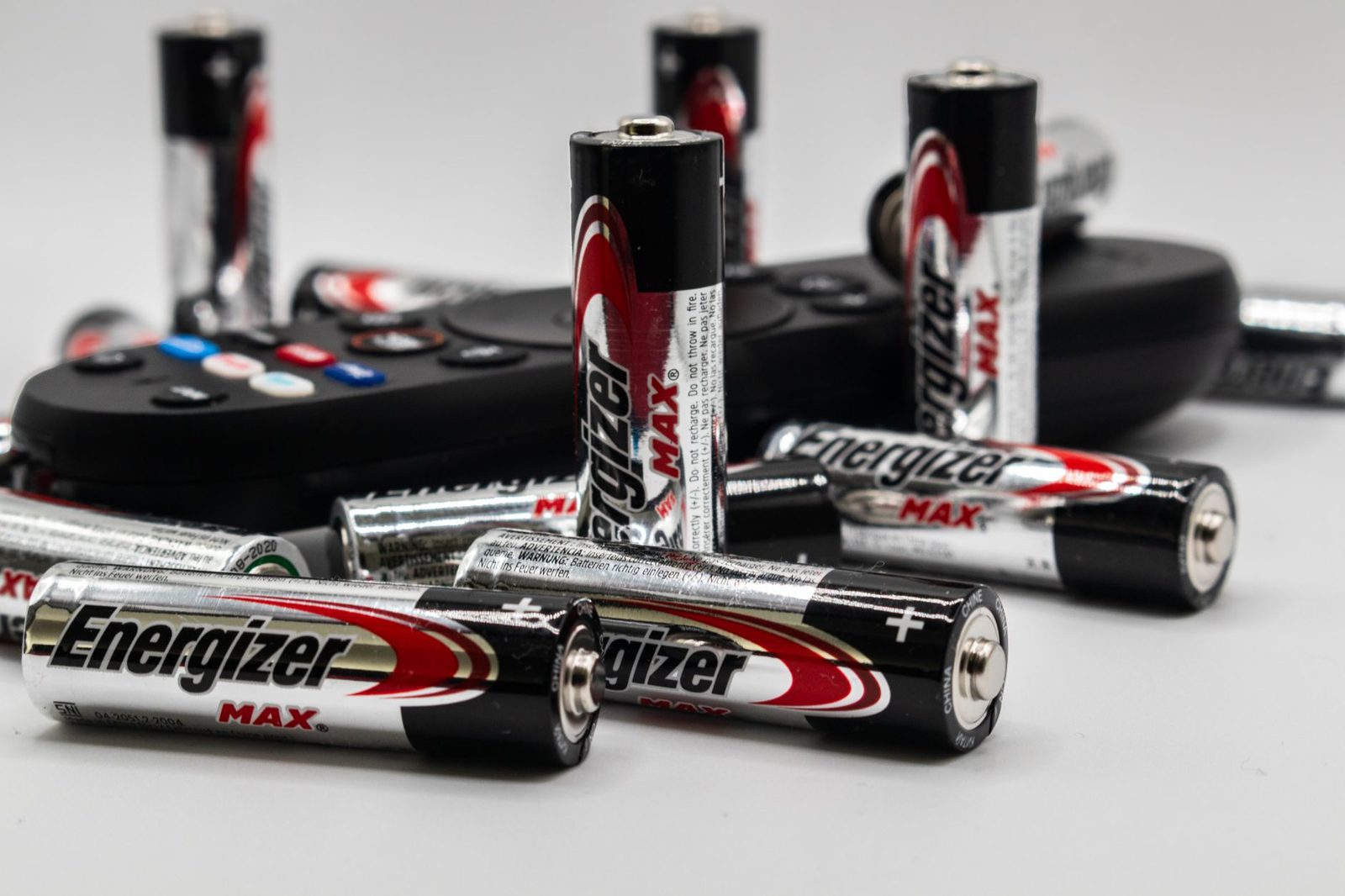 Close-up of multiple Energizer AA batteries and a remote control on a white surface.