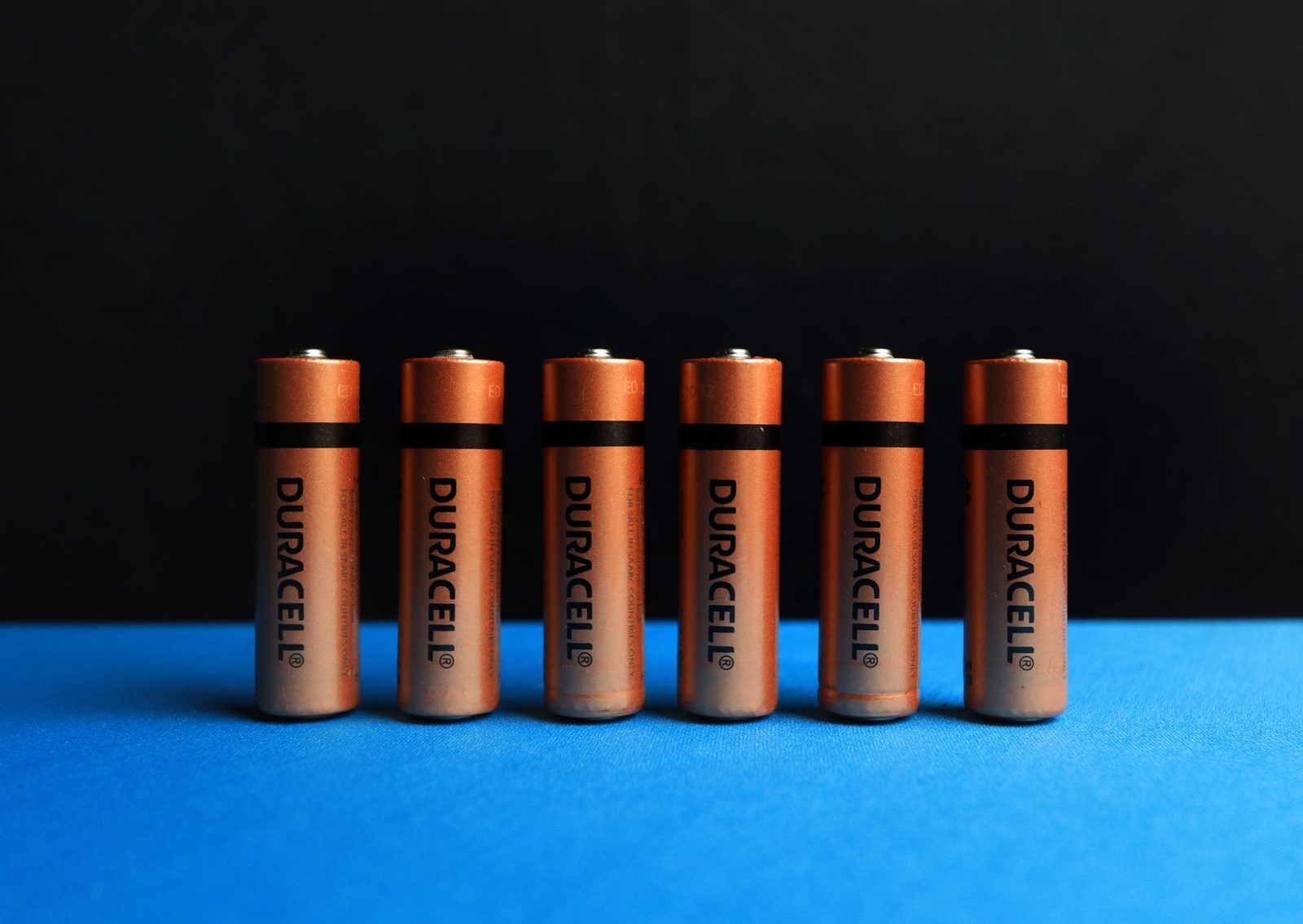 A lined up set of AA batteries with black and blue background.