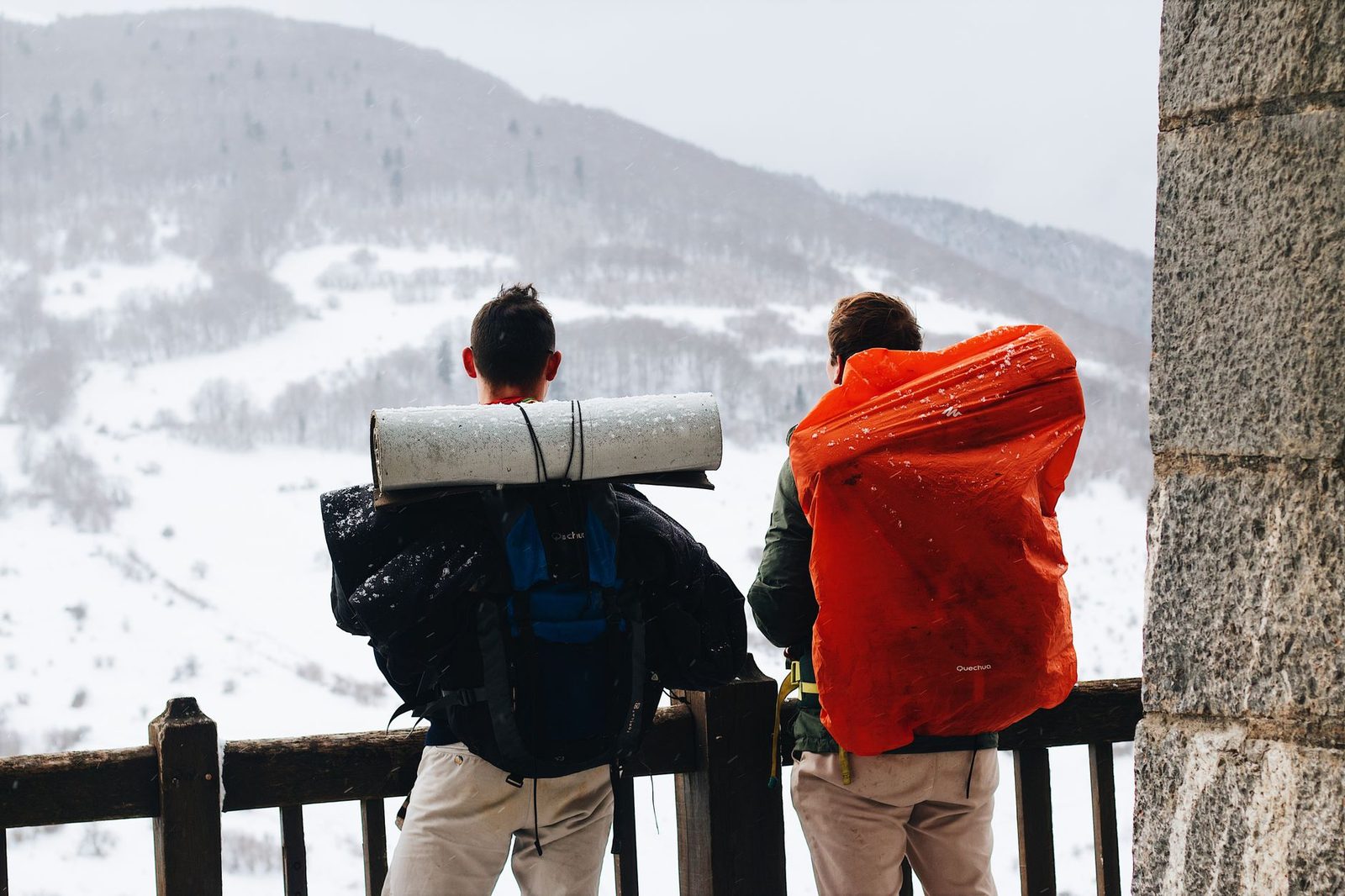 Two male hikers with backpacks enjoying a snowy mountain view in winter.