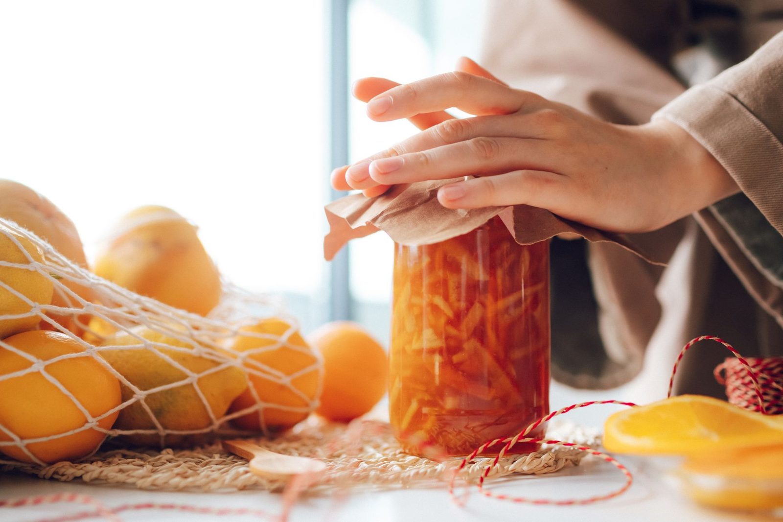 A jar of homemade orange marmalade with fresh oranges in a cozy kitchen setting.