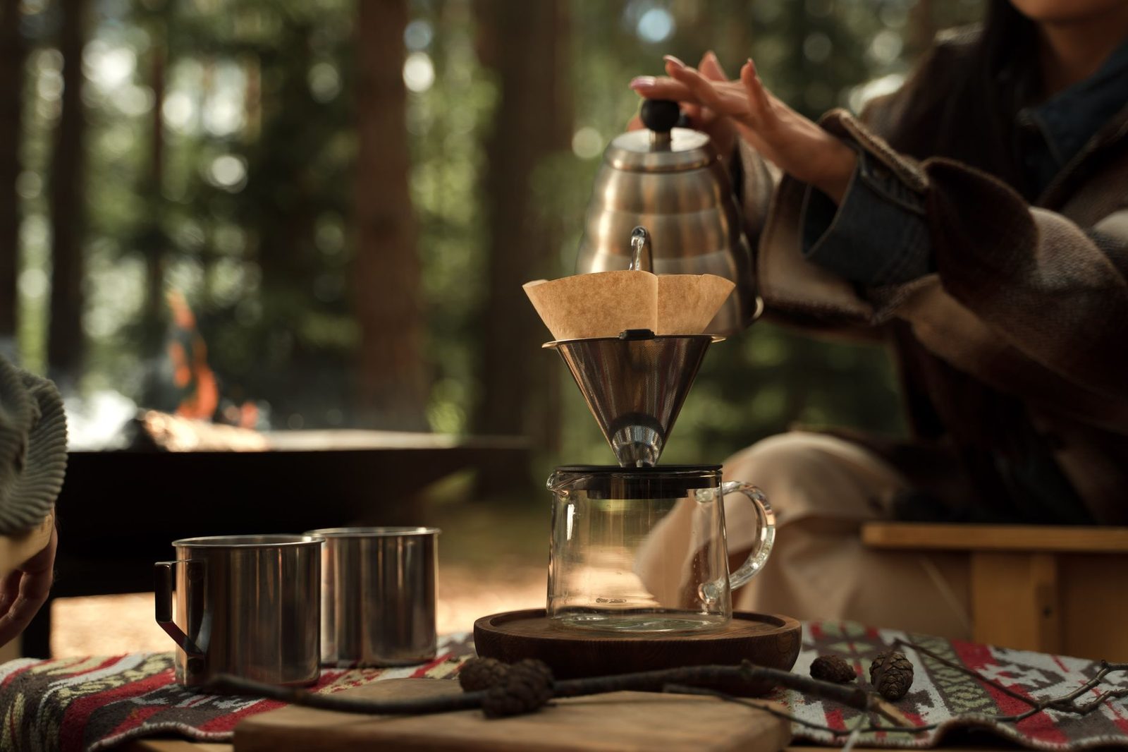 A serene outdoor scene capturing a hand brewing coffee with a pour over method, highlighting nature and simplicity.