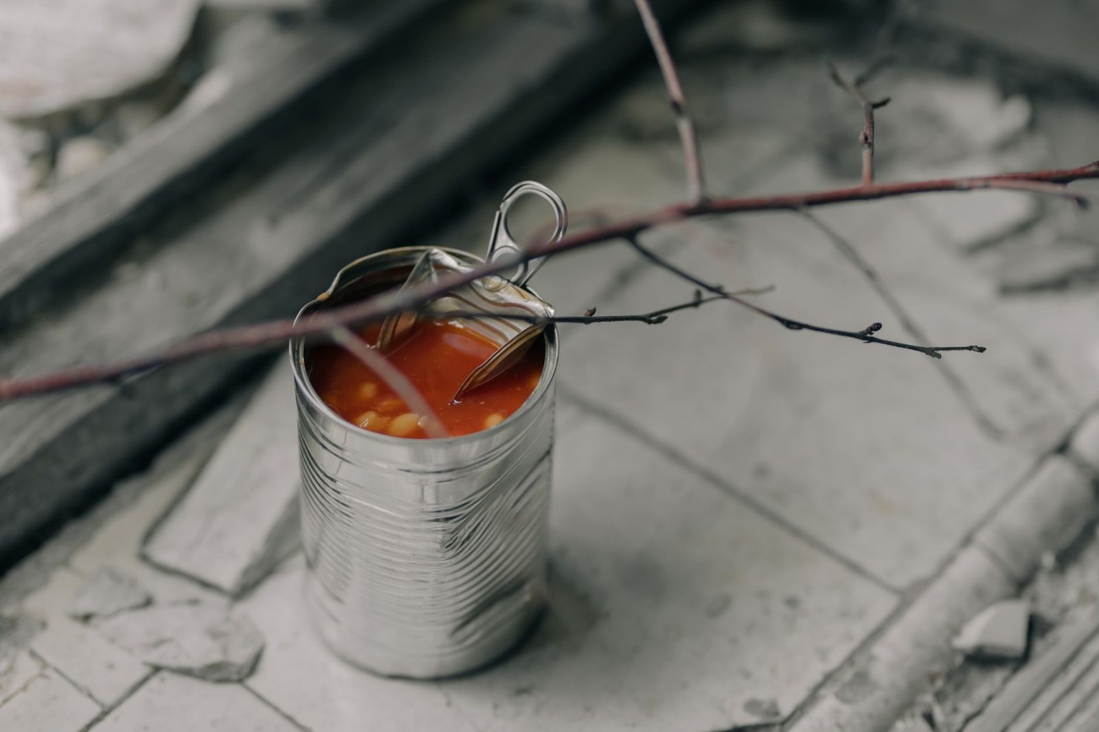 Open tin of beans in tomato sauce placed on a distressed surface with twigs, creating a rustic vibe.