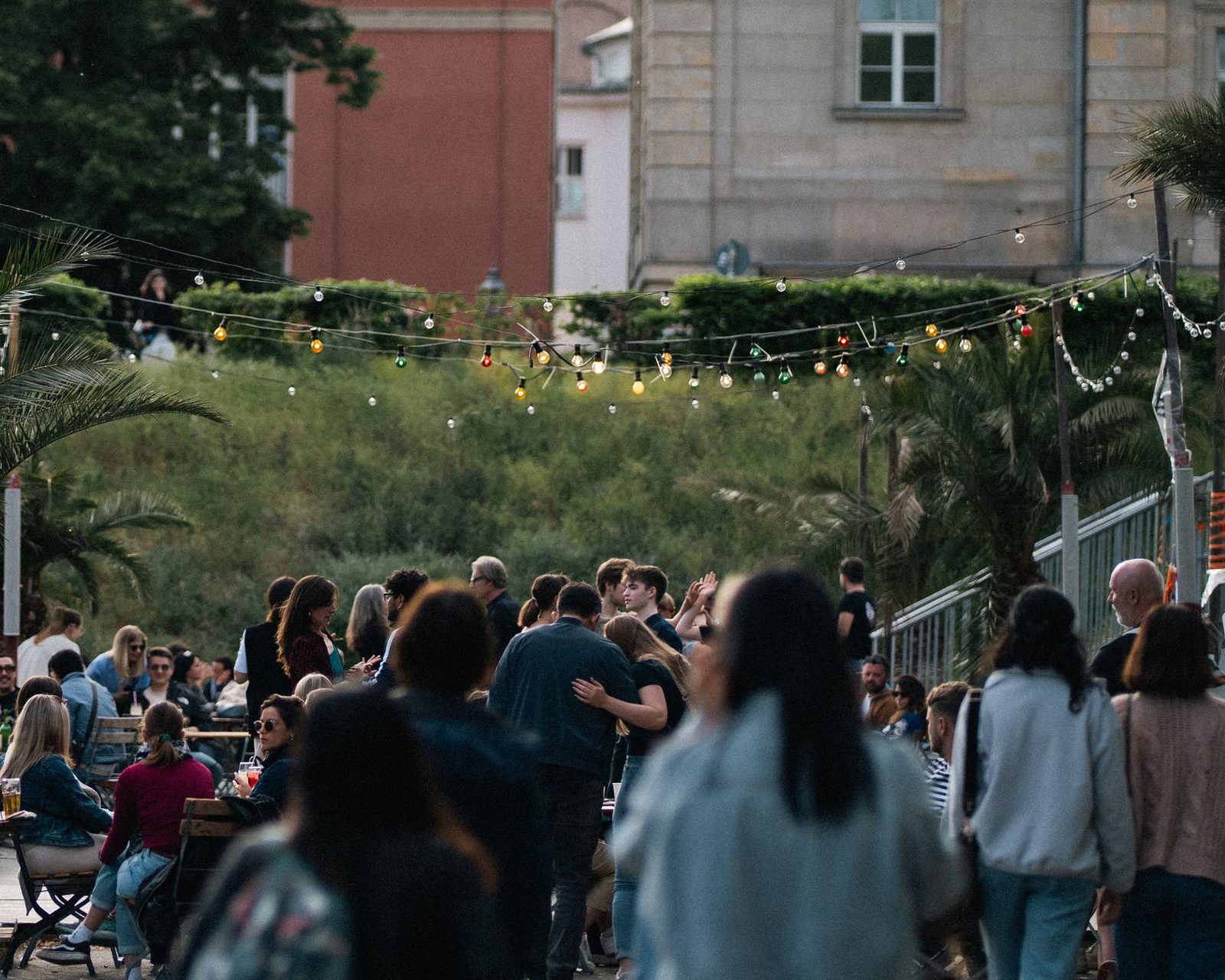 Enjoy a lively outdoor gathering with colorful lights and a diverse crowd at dusk in an urban setting.