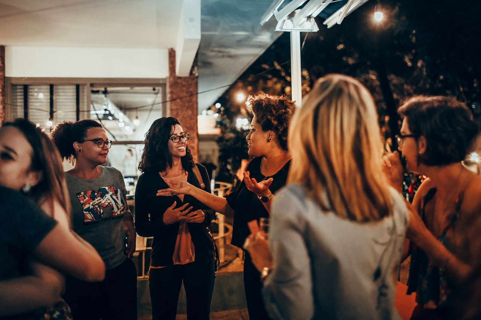 A vibrant group of women engaged in conversation during an outdoor evening gathering.