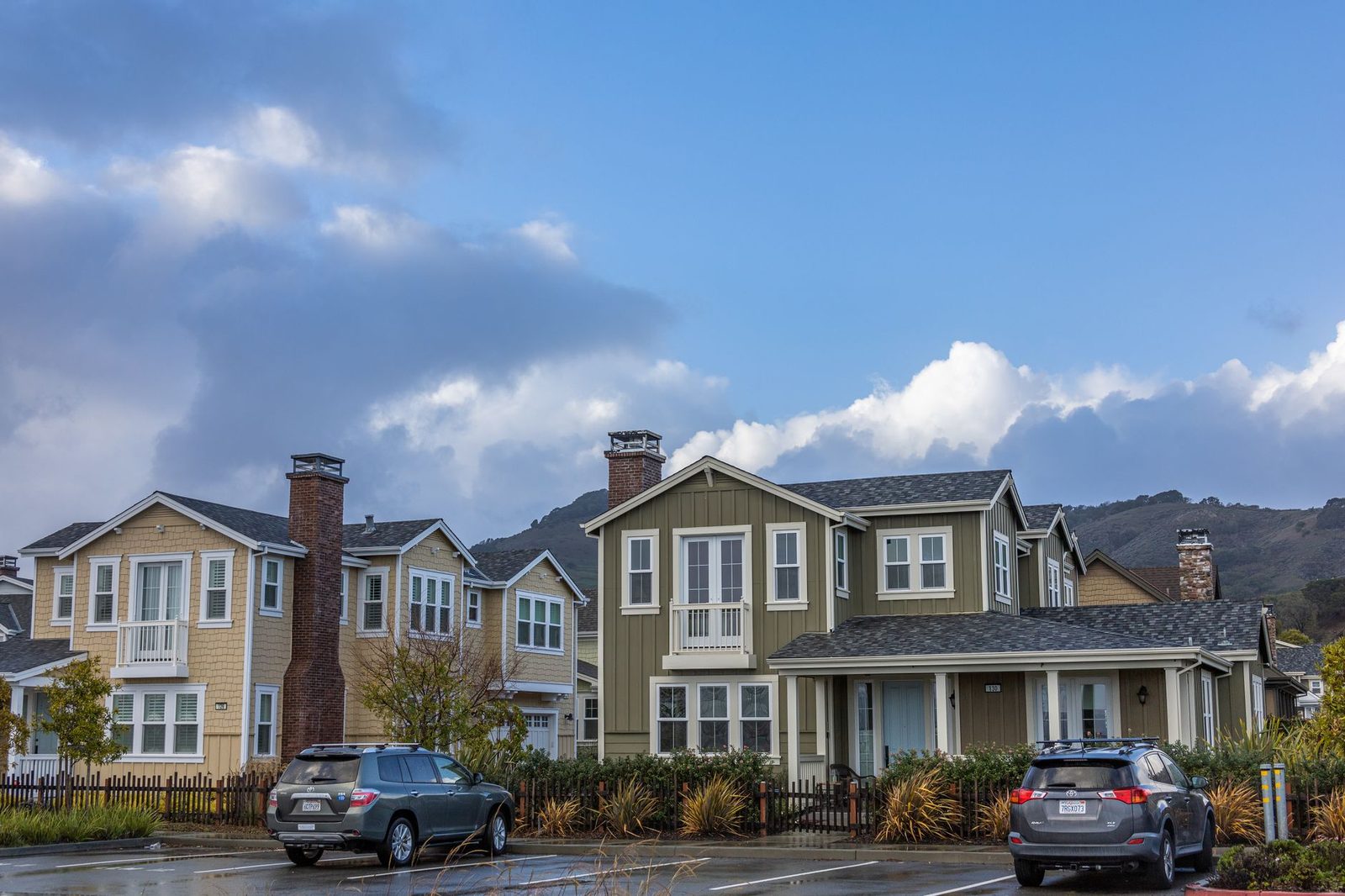 Picturesque suburban neighborhood with modern houses and parked cars under a partly cloudy sky.