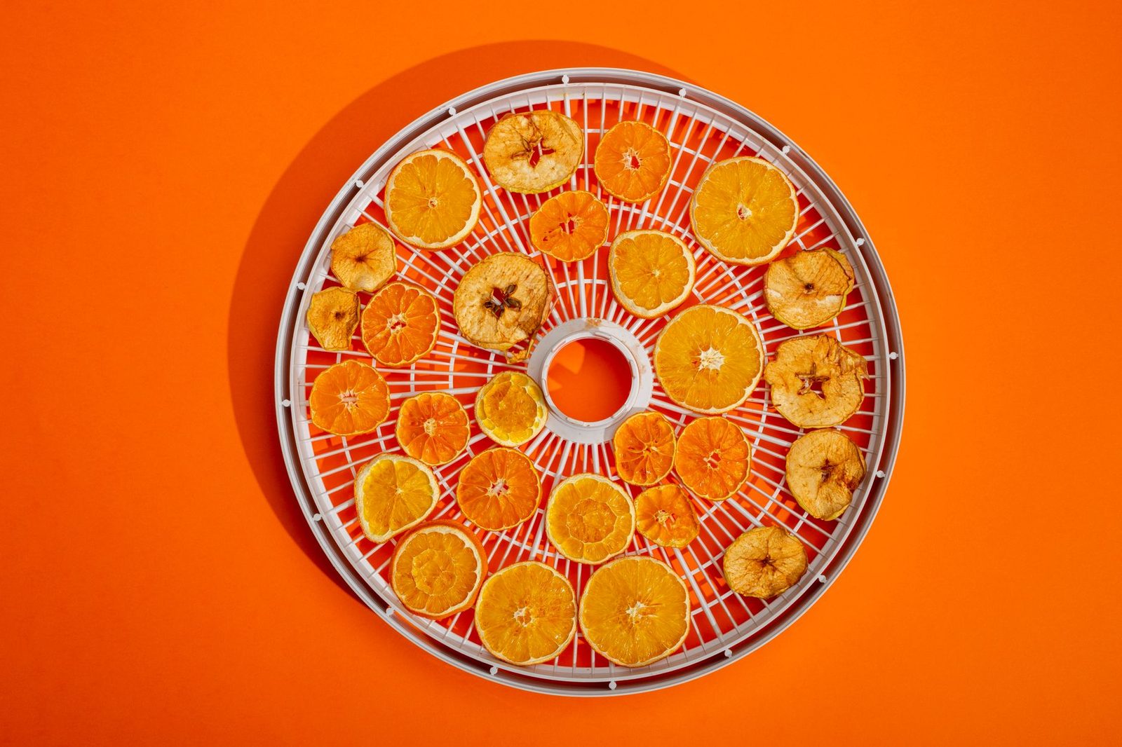 A collection of dried citrus slices on a round drying rack with a bright orange background.