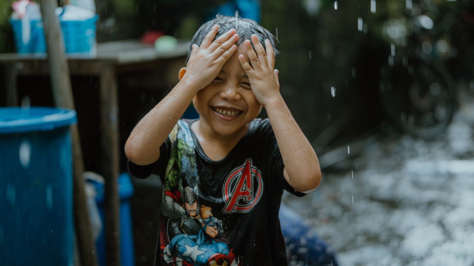 Smiling child enjoying rain in casual attire, embracing carefree childhood moments.