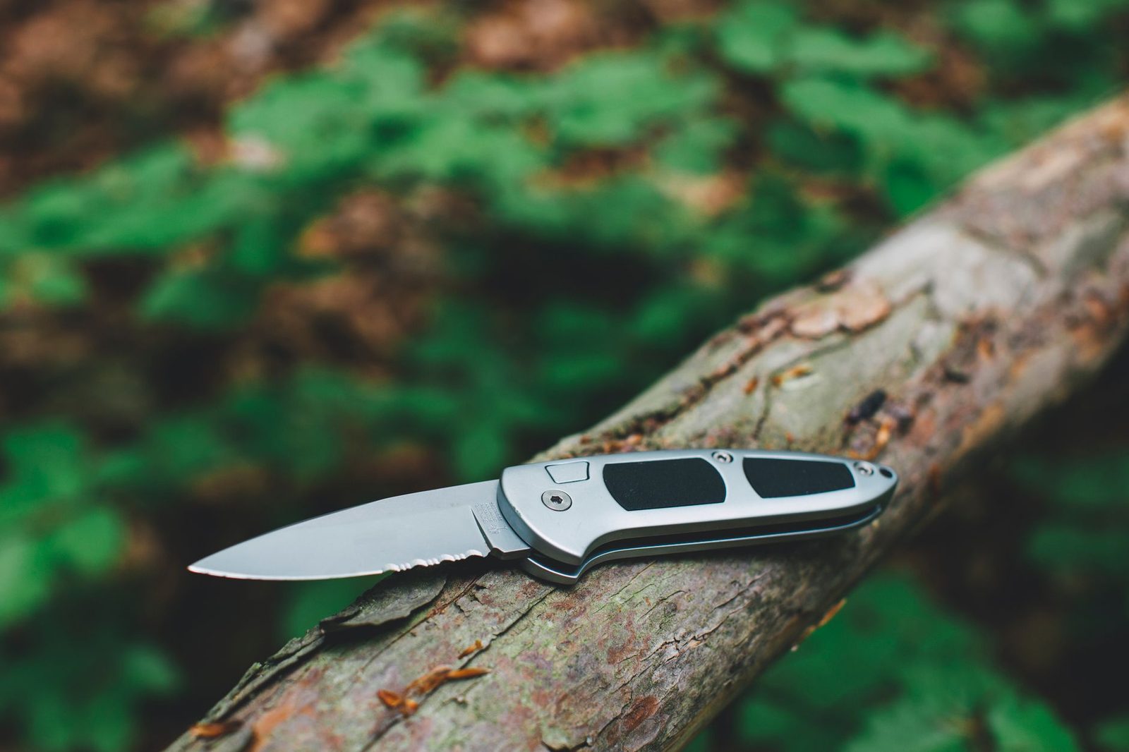 Close-up of a stainless steel pocket knife resting on a wooden log in nature.