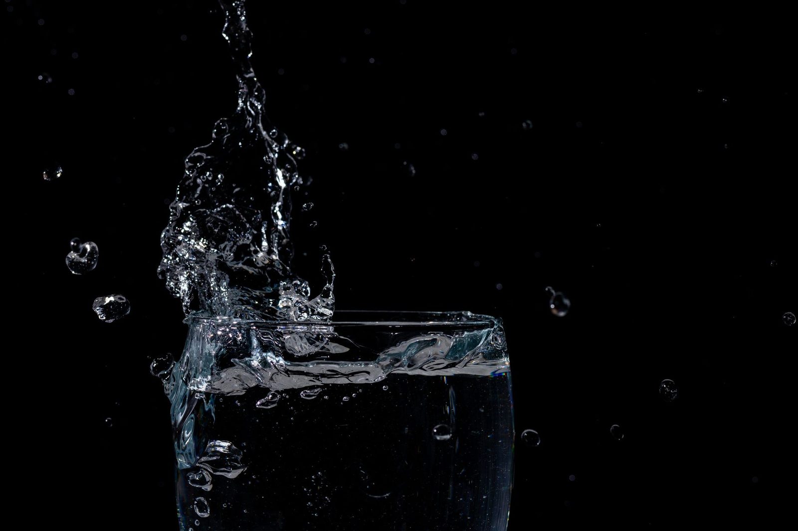 Close-up of water splashing in a glass against a black background.