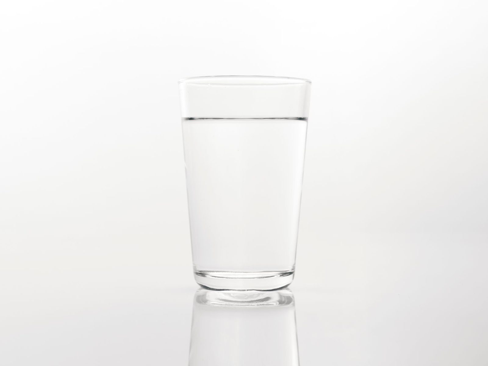 A simple close-up of a clear glass of water on a reflective white background.