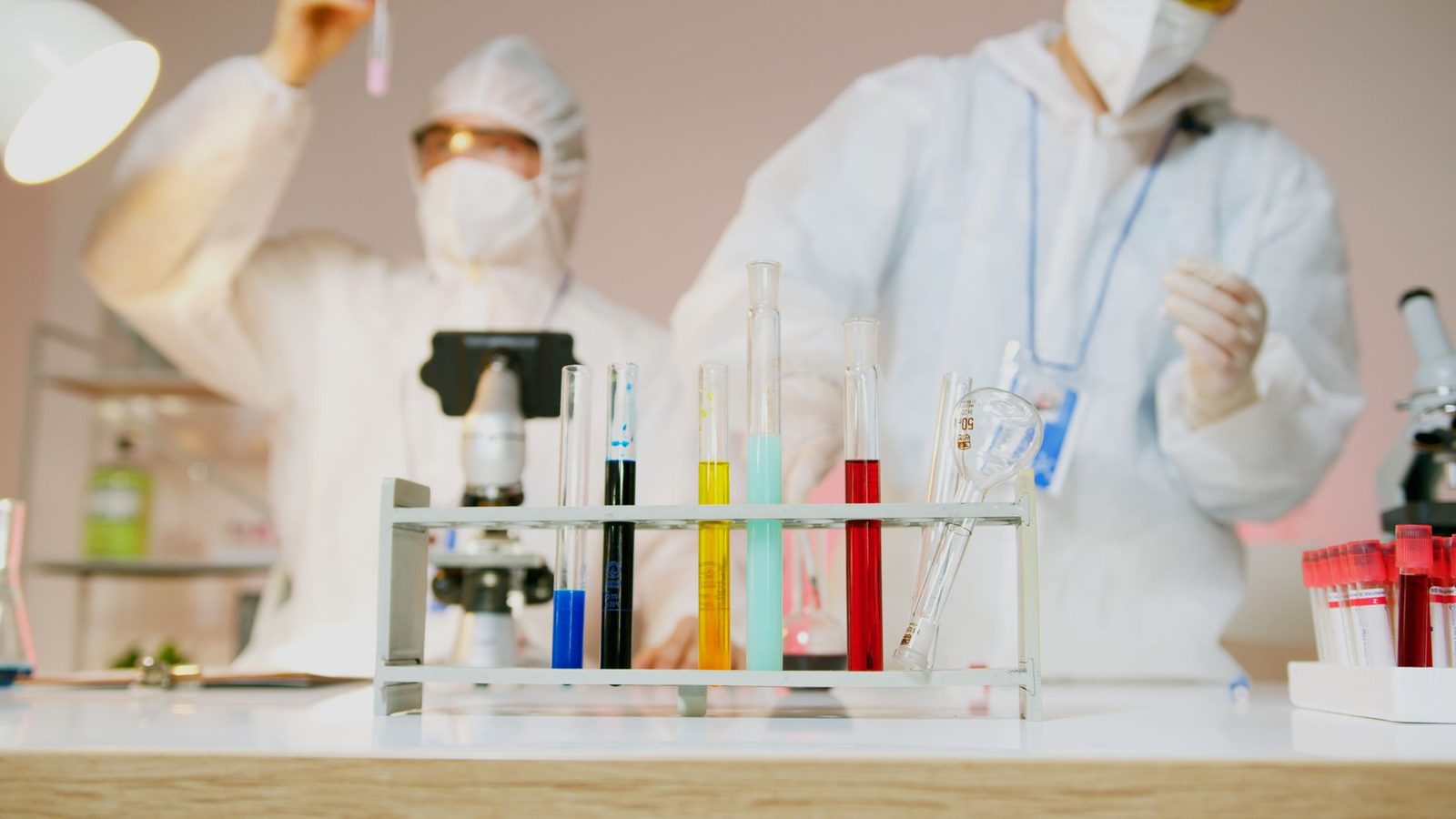 Two scientists with protective gear working with test tubes in a modern lab setup.