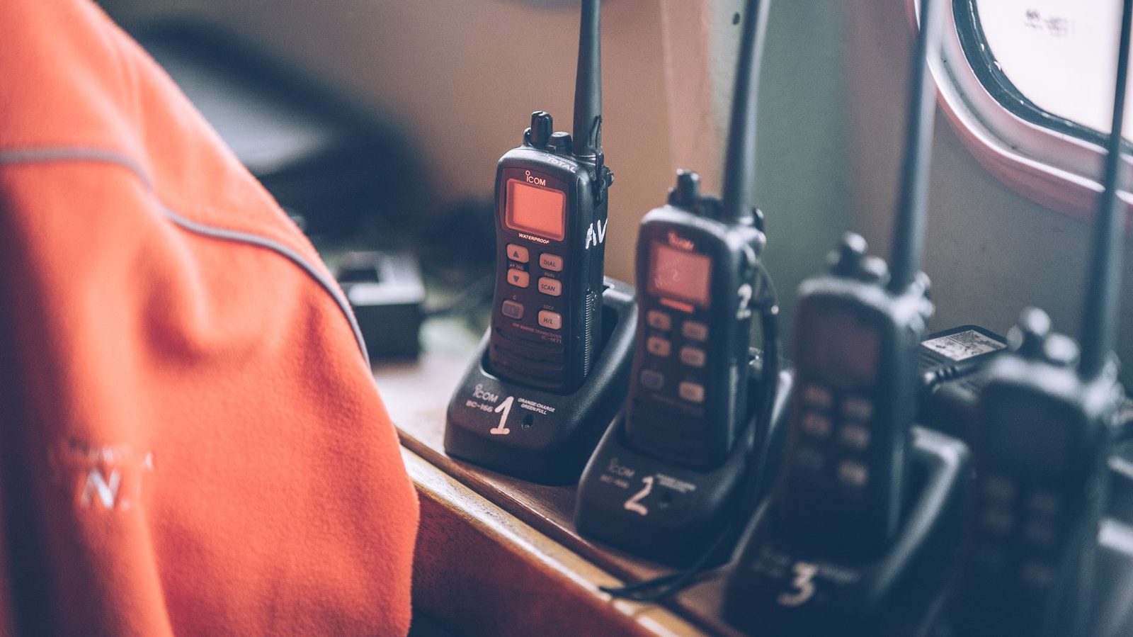 Four wireless walkie talkies in charging stations on a wooden dock indoors.