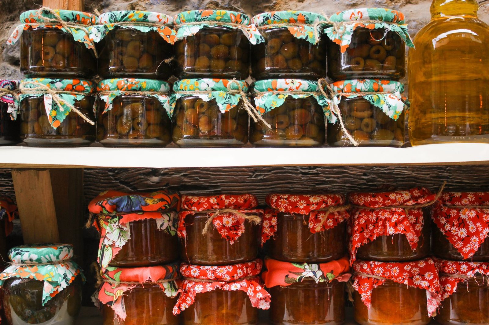 Variety of colorful homemade preserves and pickles in jars with fabric covers.