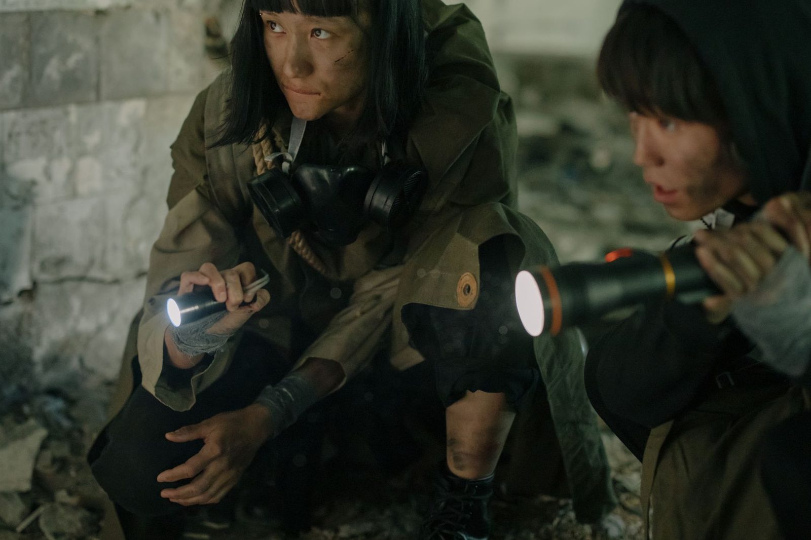 Two individuals exploring a dark, decaying urban environment with flashlights.