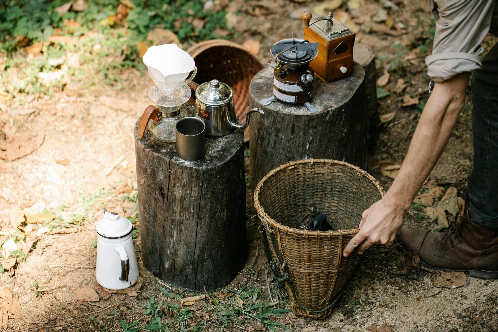 From above of crop anonymous male farmer with bucket on pathway against coffee kettle and gas burner on stumps