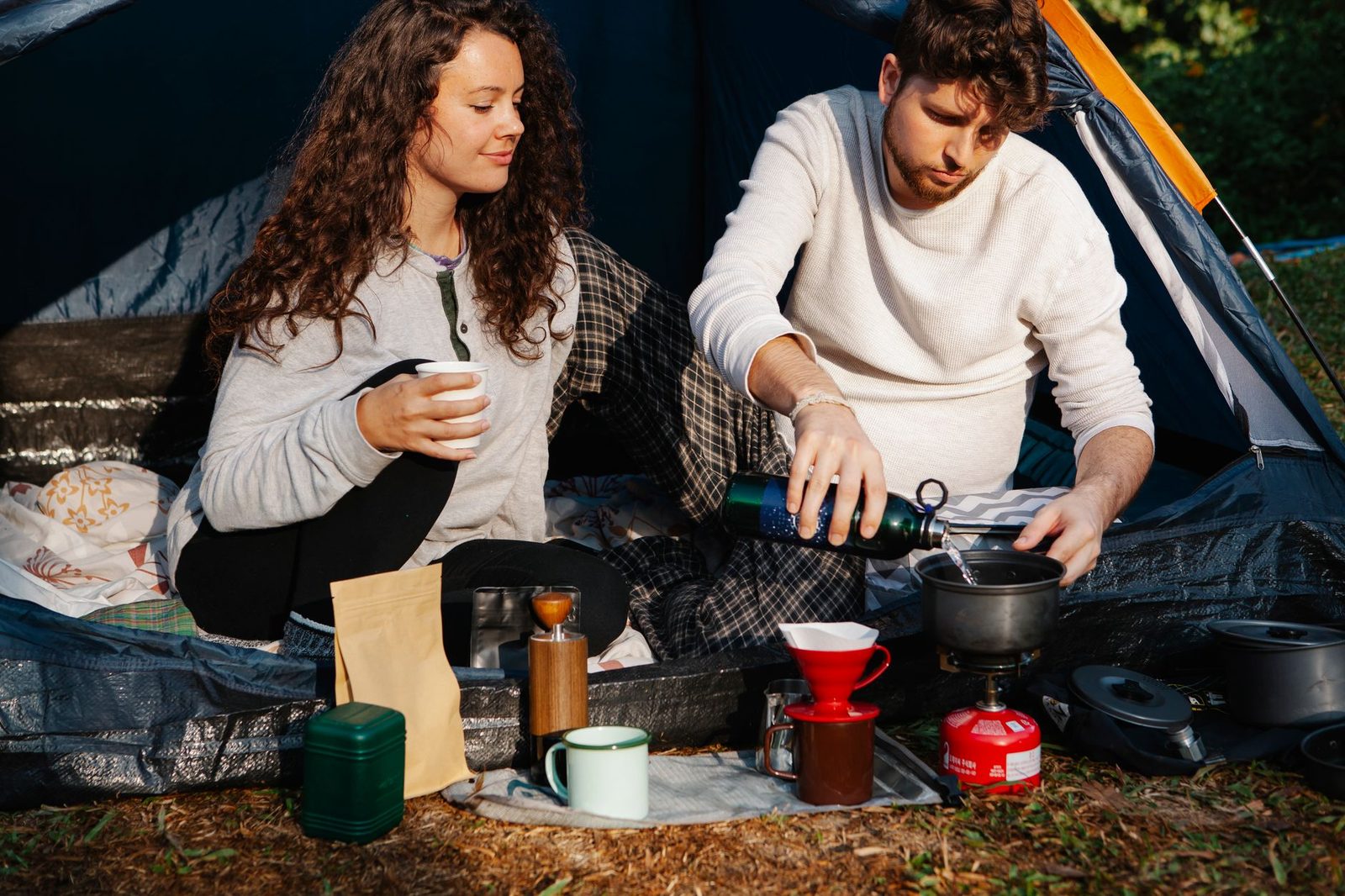 Crop male tourist pouring water into pot while preparing coffee near female beloved in tent