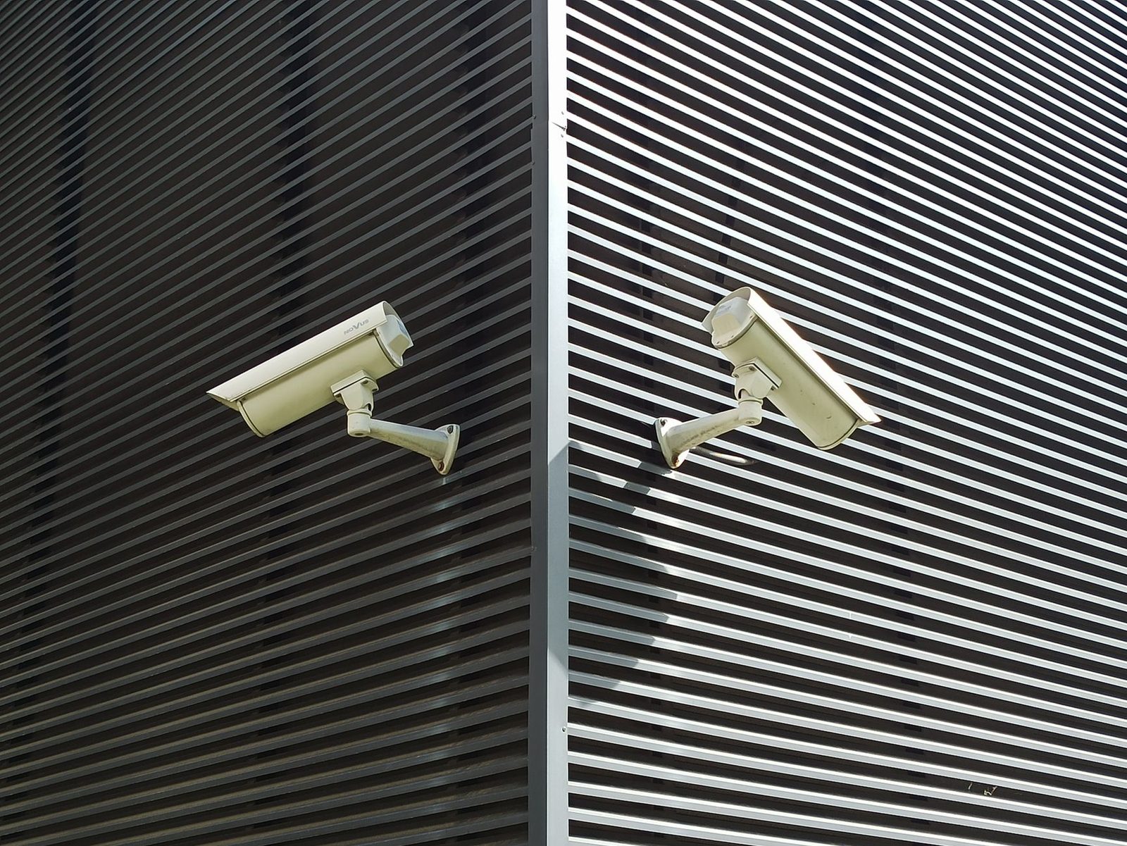 Two security cameras mounted on a slatted wall for surveillance.