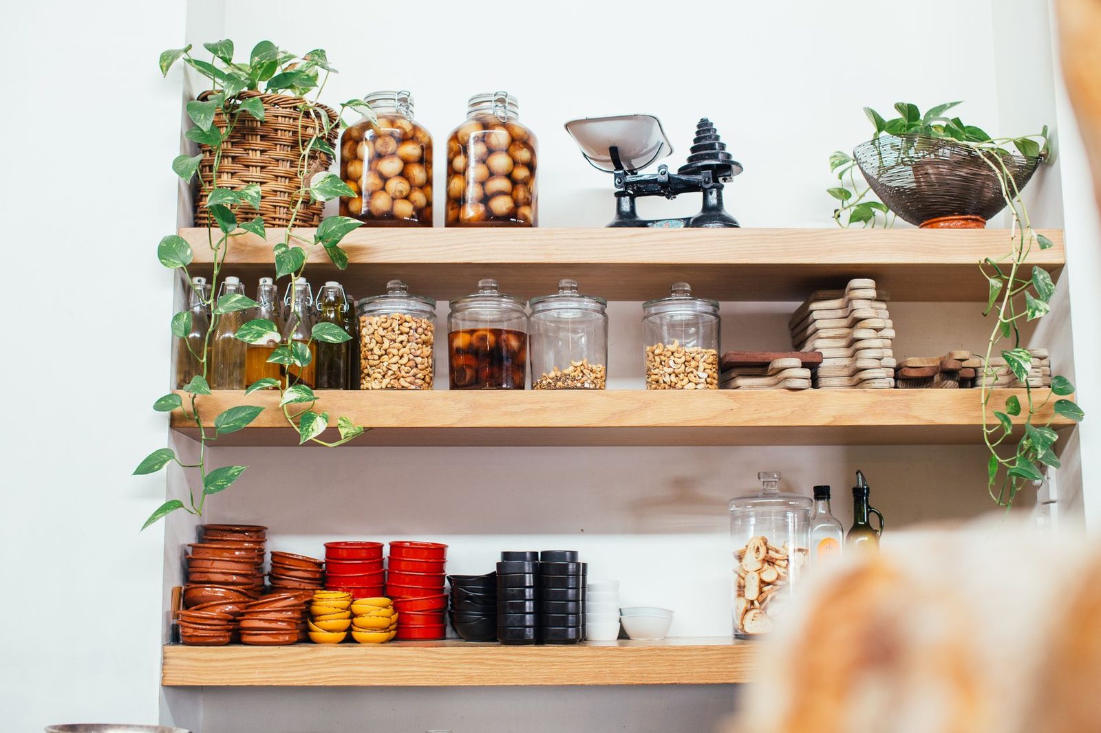 Timber shelves with many glass jars filled with nuts near green potted plants and plastic containers