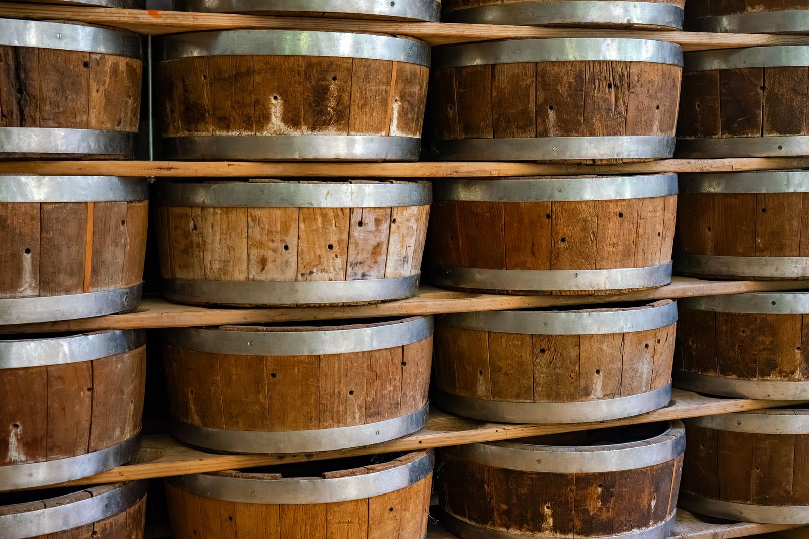 Close-up view of wooden barrels stacked on shelves inside a winery storage area.