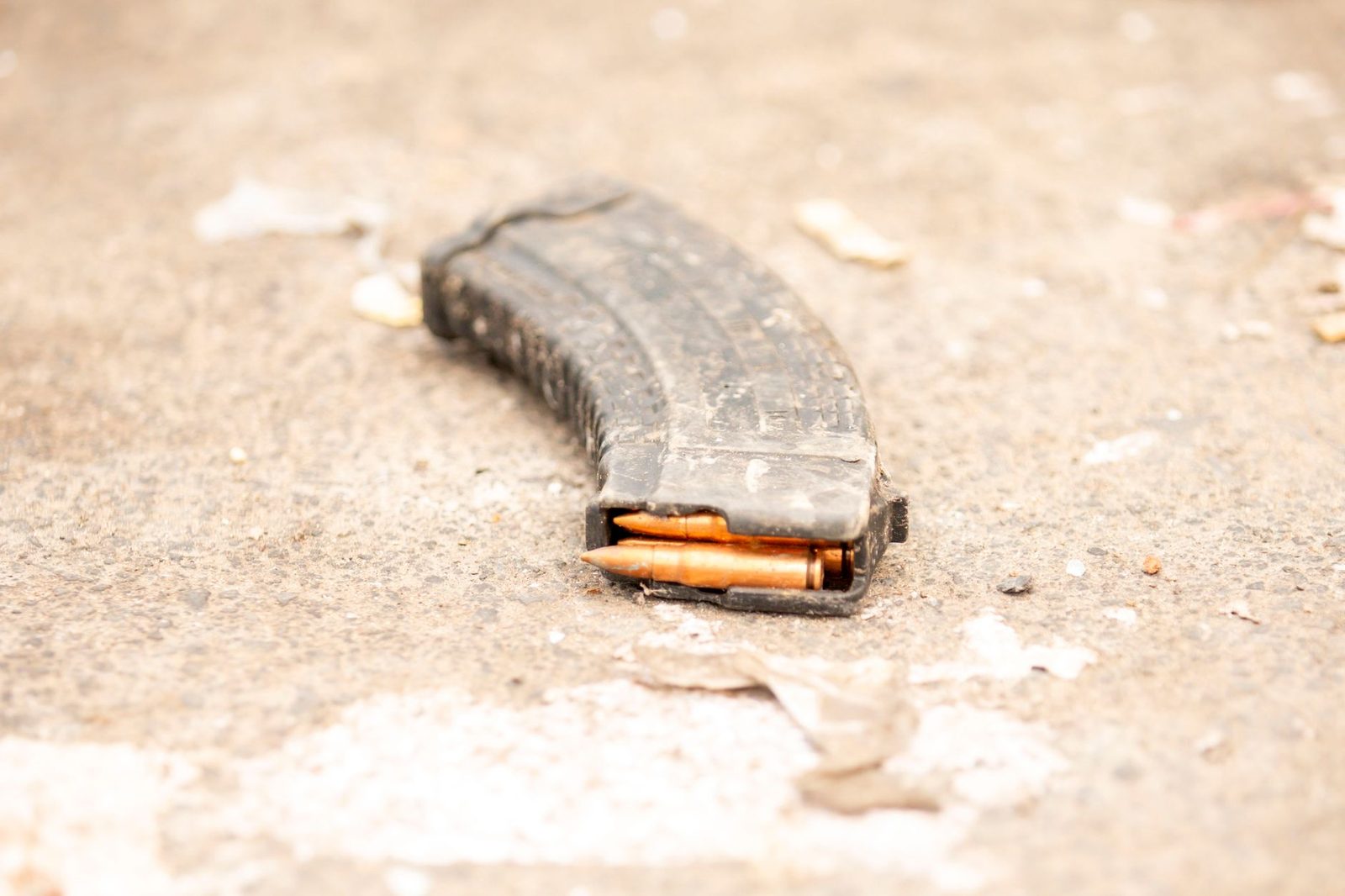 Rifle magazine with visible bullets lying on a rough concrete surface.