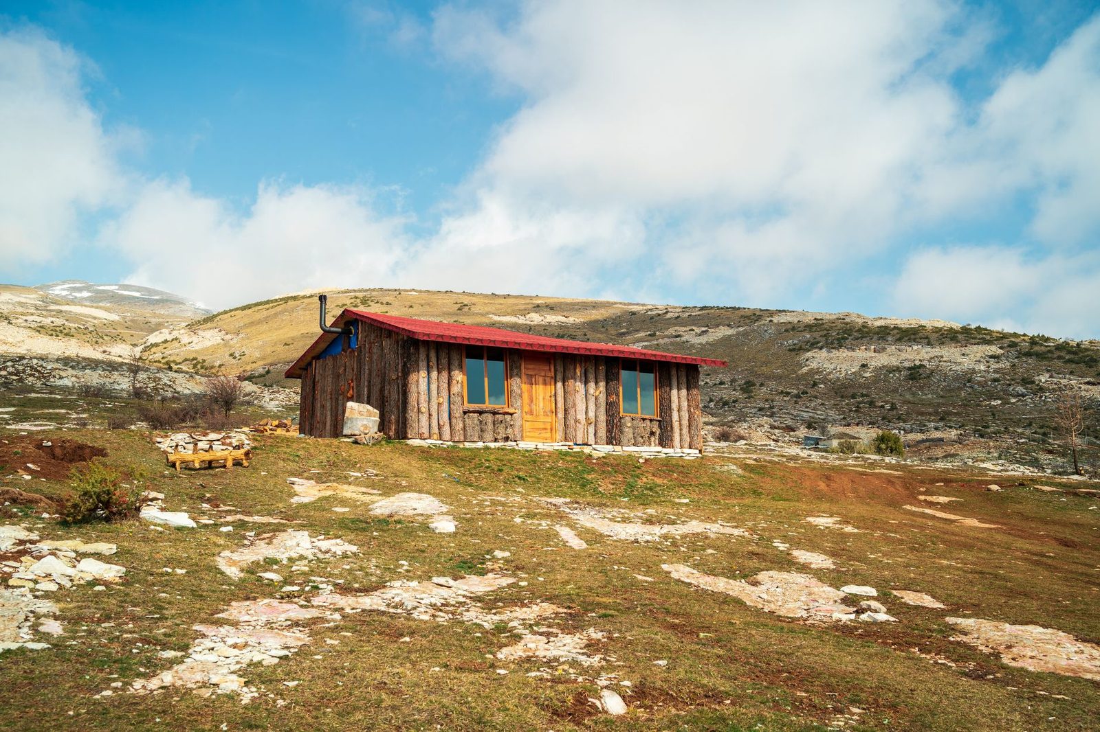 A rustic wooden cabin on a hill under a clear blue sky with scattered clouds.