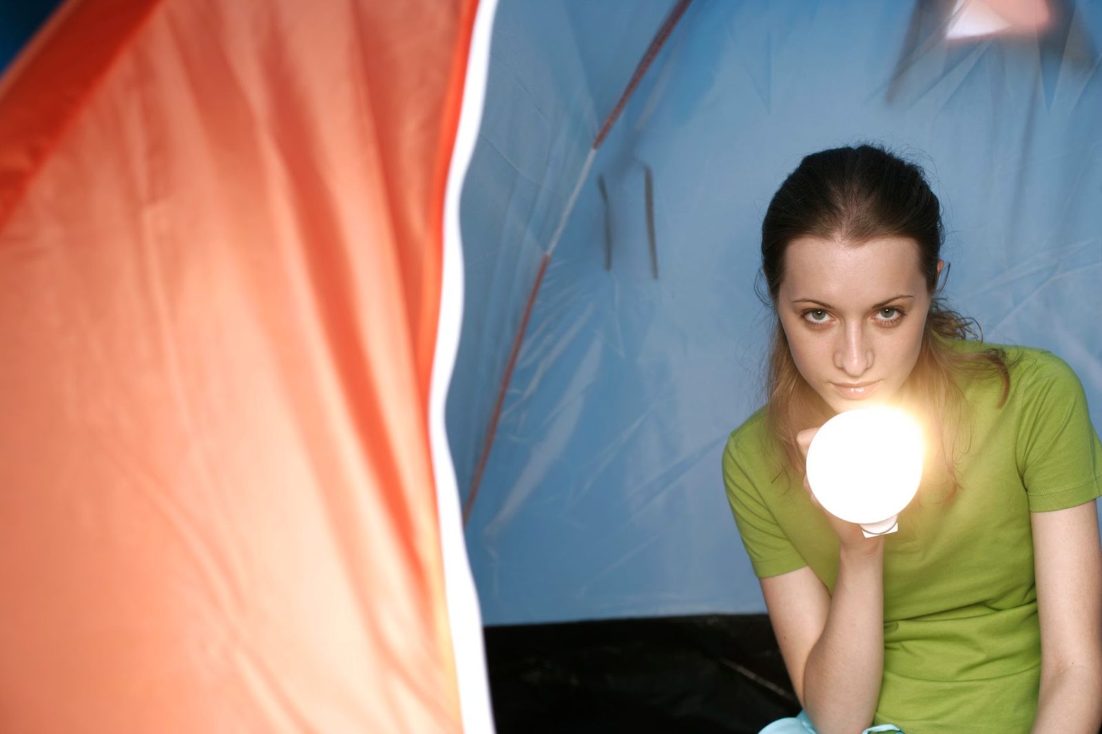 Woman with brown hair holds a flashlight inside a colorful tent, creating an adventurous vibe.