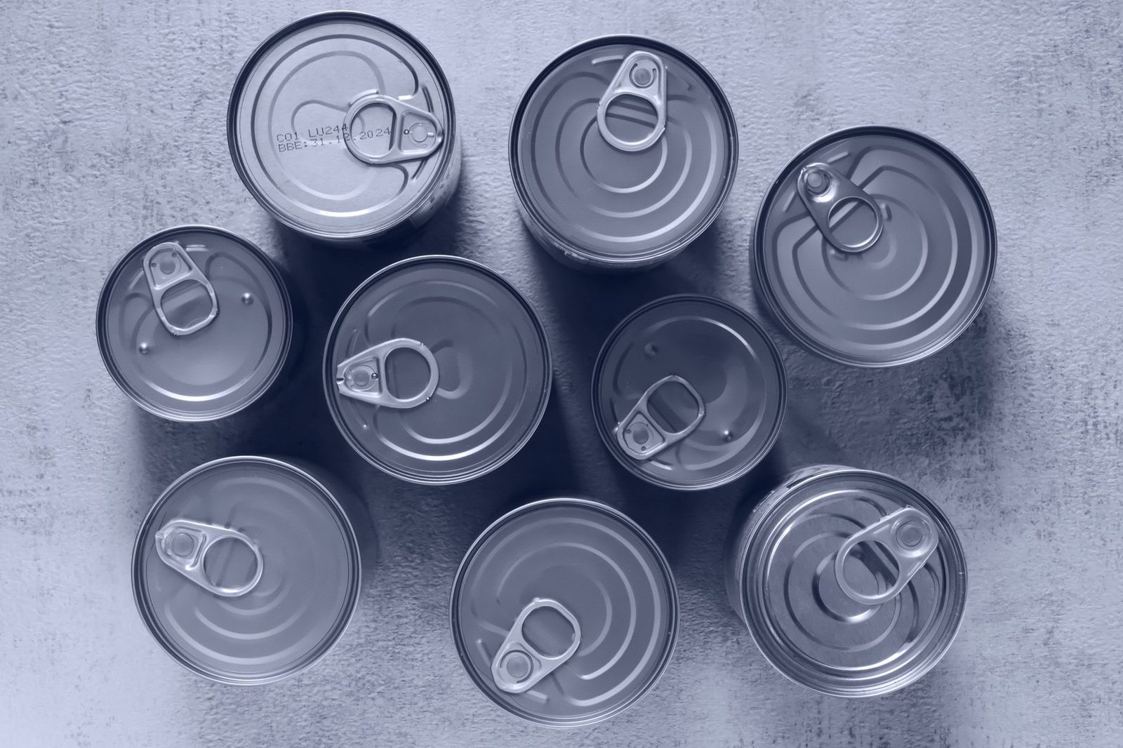 High-angle shot of canned food tins arranged on a rough surface, emphasizing texture and symmetry.