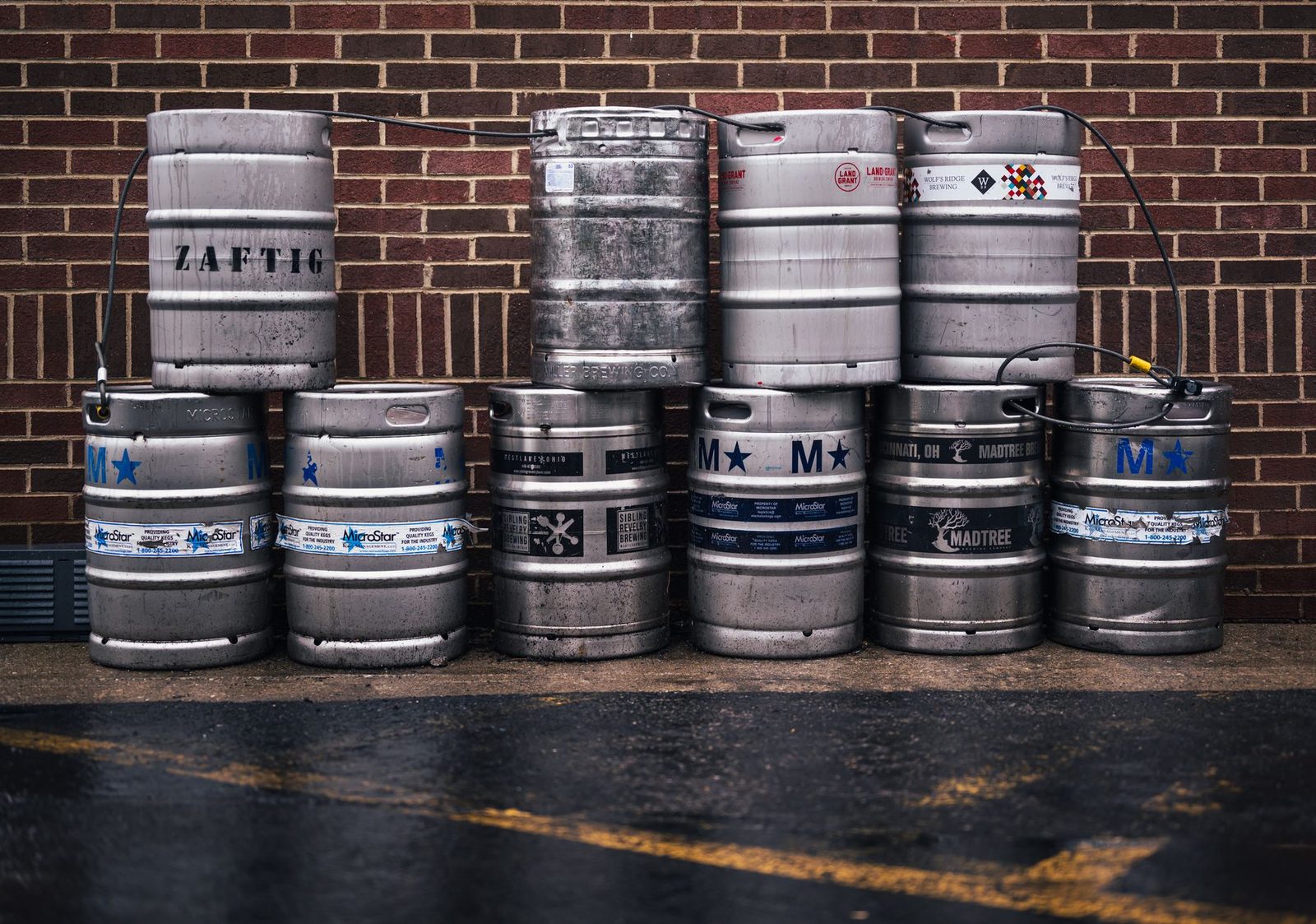 Row of metallic beer kegs stacked outside a brick wall, showcasing brewing industry.