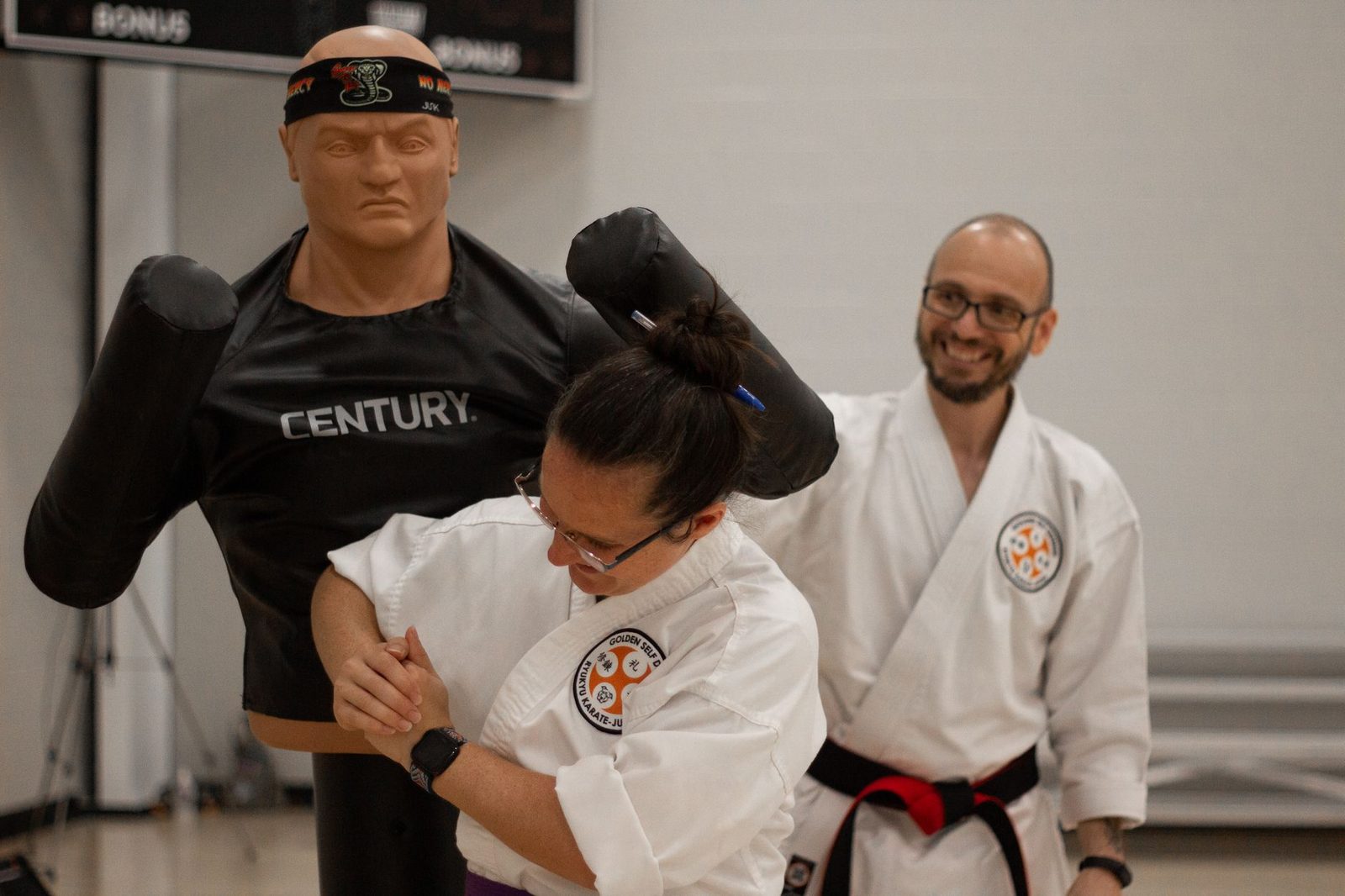 Martial arts training with a karate mannequin and an instructor guiding a student in self-defense techniques.