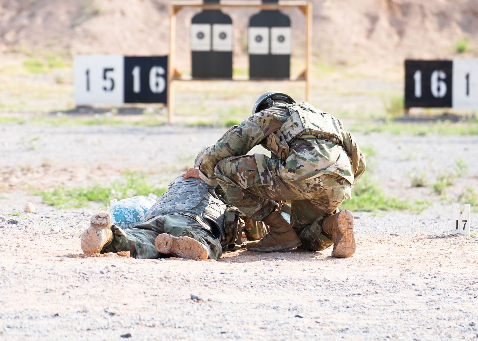 Two soldiers in military uniforms participate in a training exercise at a shooting range.