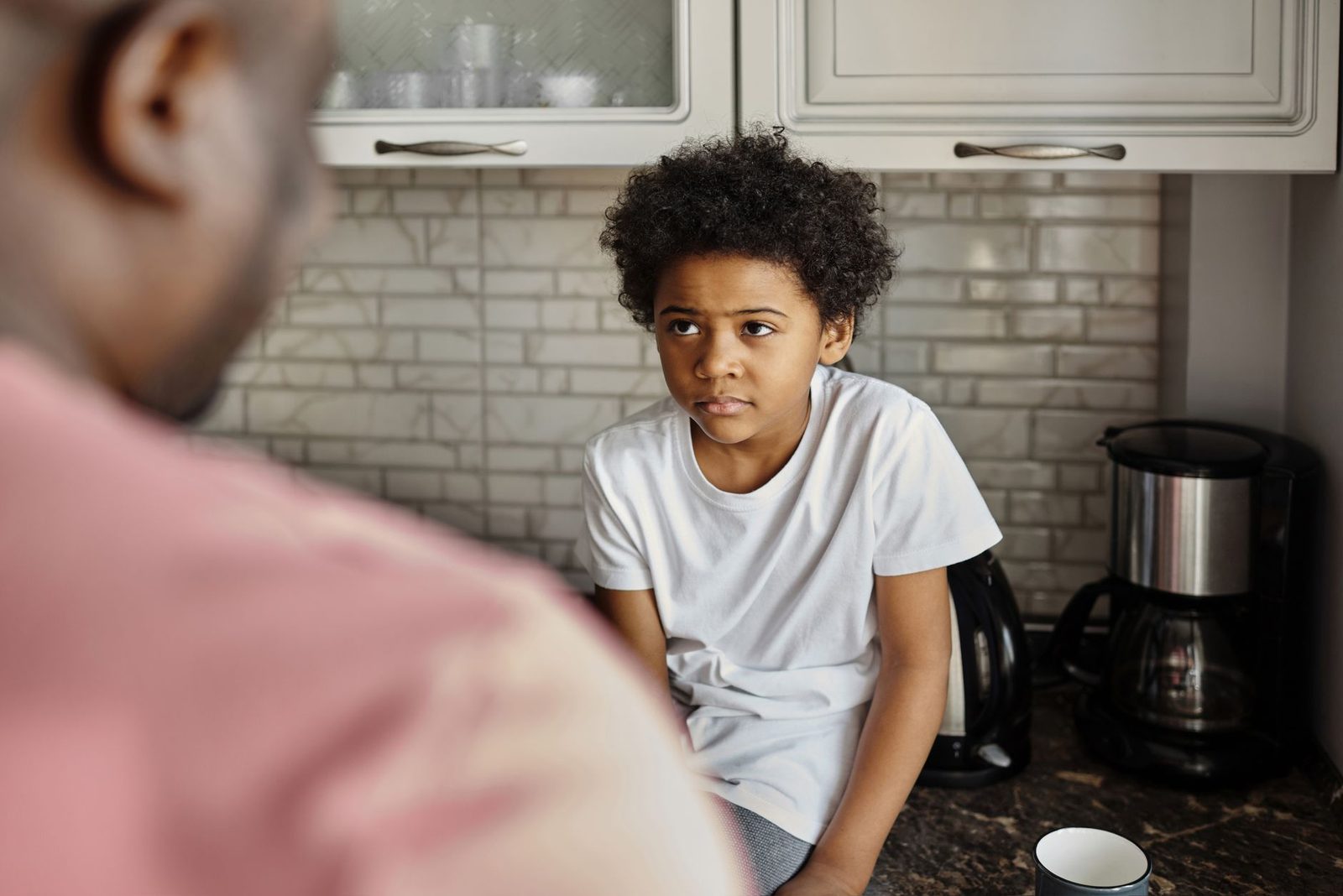A father and son having an emotional conversation in a cozy kitchen setting.