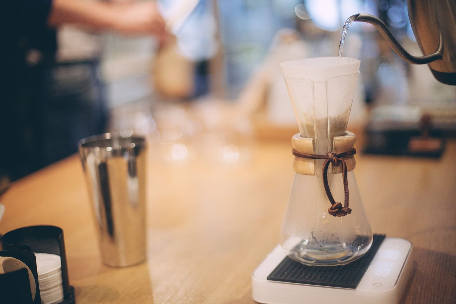 Barista making coffee using drip kettle pouring water into glass flask with paper filter with grounded coffee beans