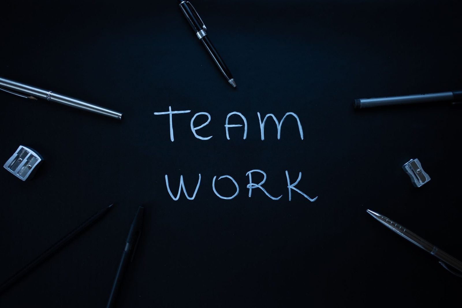 Arrangement of office supplies around teamwork text on black background.