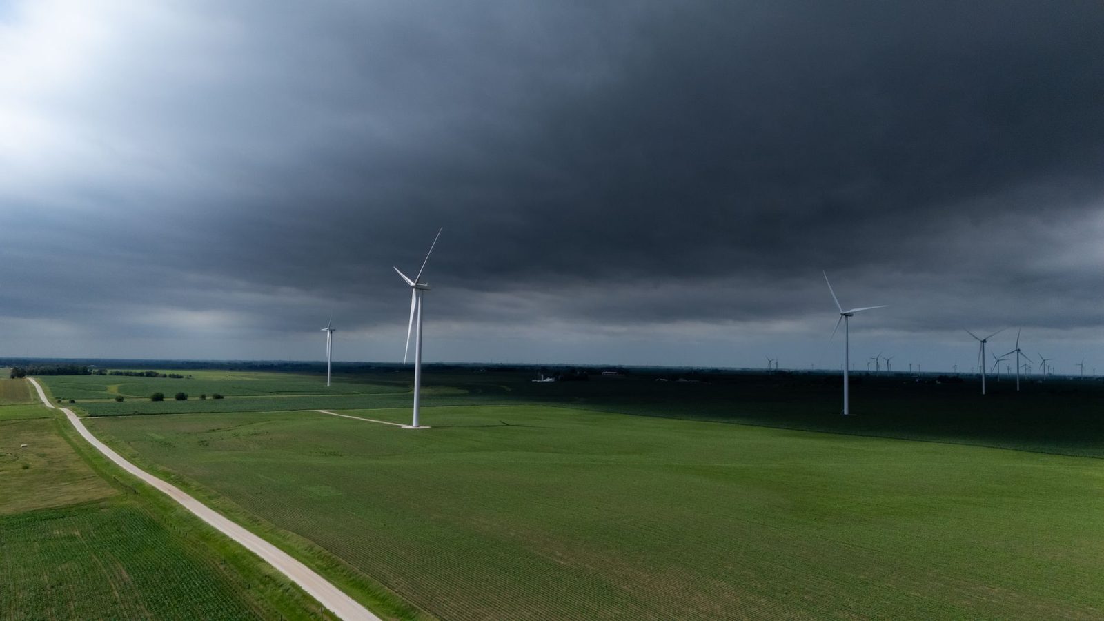 A stormy sky looms over a vast green landscape with wind turbines generating renewable energy.
