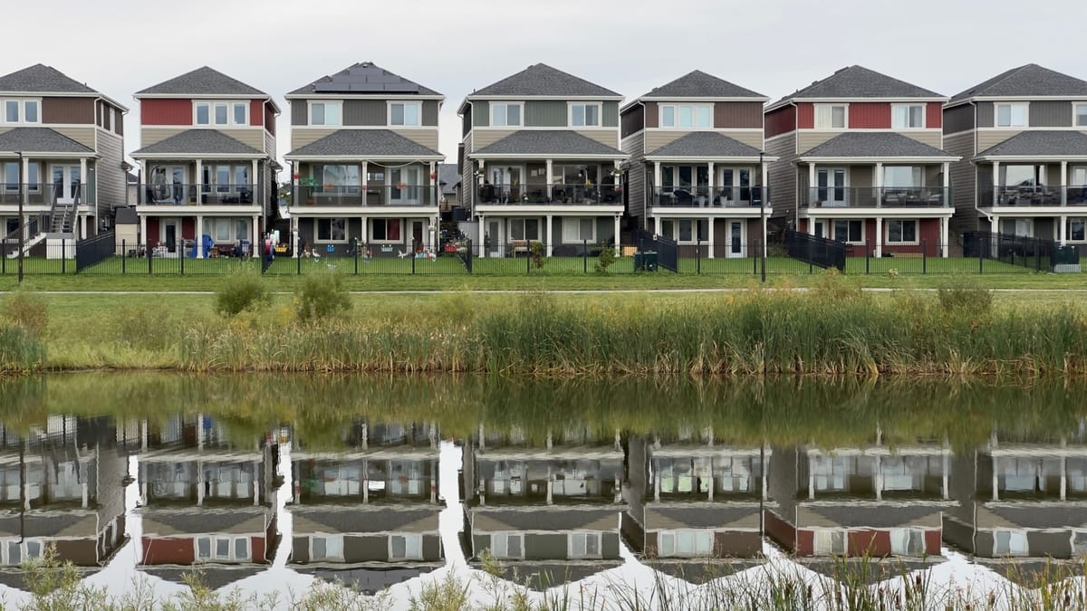 A row of modern houses reflected in a calm pond, showcasing serene suburban architecture.