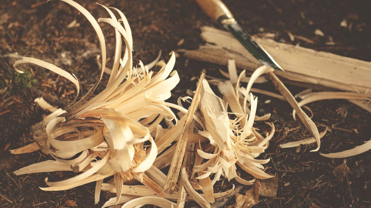 Woodworking knife and wood shavings on ground, showcasing craftsmanship in a rustic outdoor environment.