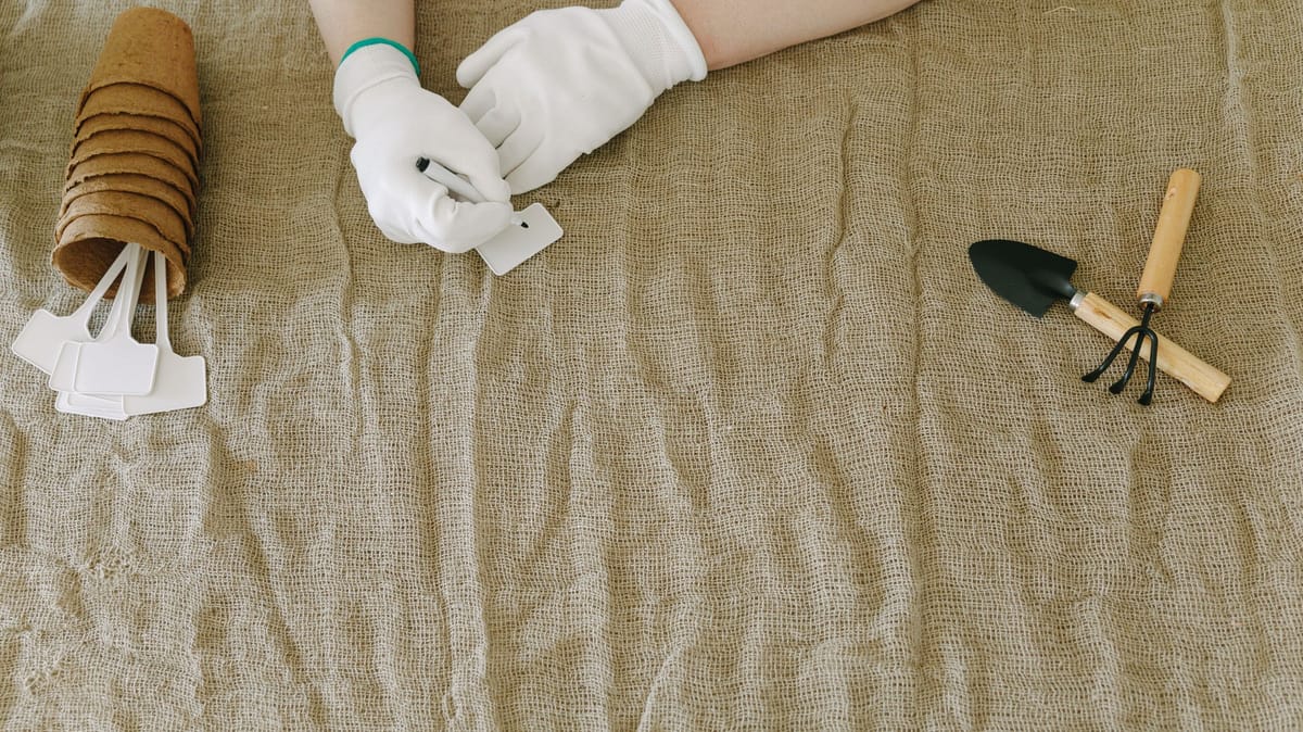 Person preparing gardening tools and labels on burlap surface, wearing gloves.