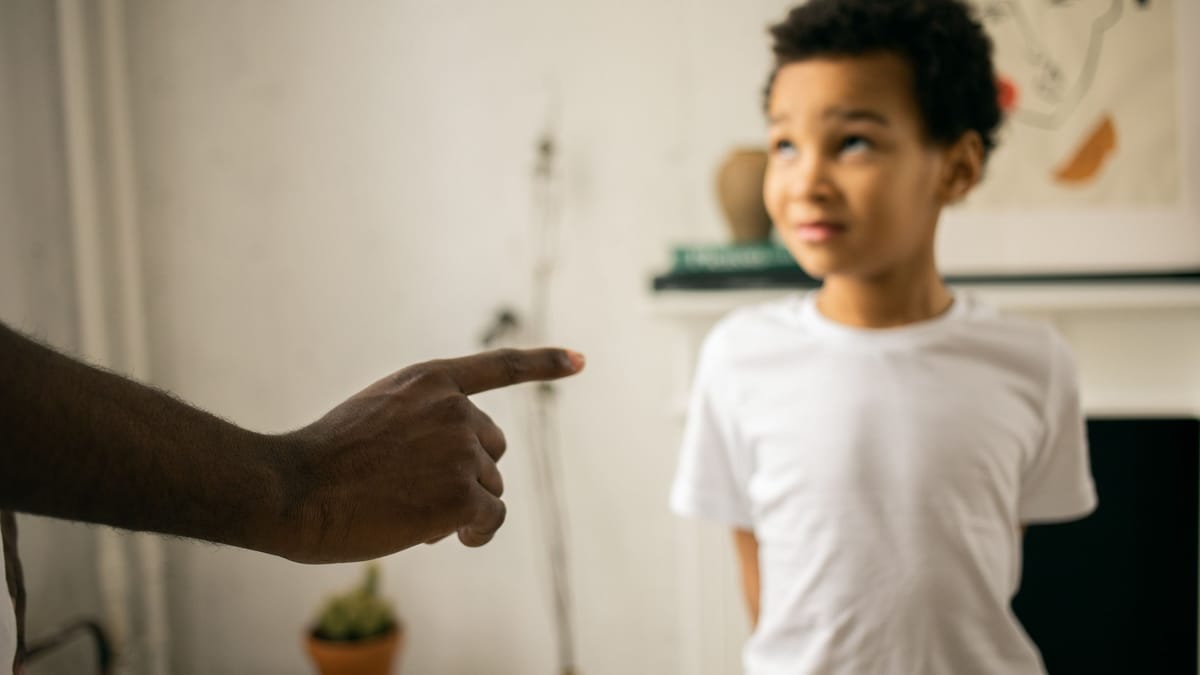 Crop unrecognizable strict black man scolding and disciplining guilty attentive little son standing with hands behind back and looking up