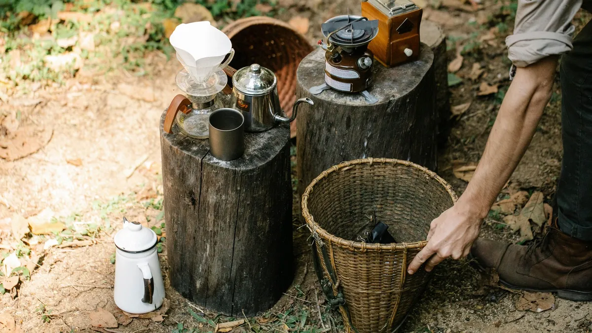 From above of crop anonymous male farmer with bucket on pathway against coffee kettle and gas burner on stumps