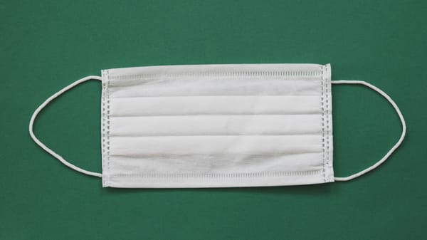 White surgical mask placed against a vibrant green background for health safety themes.