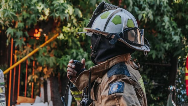 Firefighter in full protective gear using a radio outdoors.