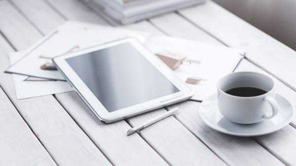 White tablet with stylus and coffee cup on modern office desk setup.