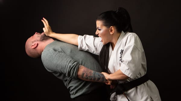 A woman in karate attire defends herself against a man in a martial arts demonstration.