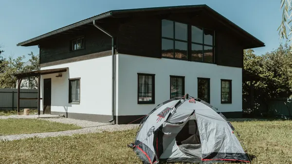 A modern two-story house with a pitched roof and a camping tent in the grassy garden.